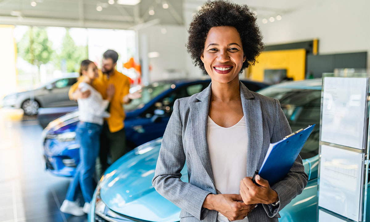 Woman stands with couple blurred in the background at Guest Auto Sales